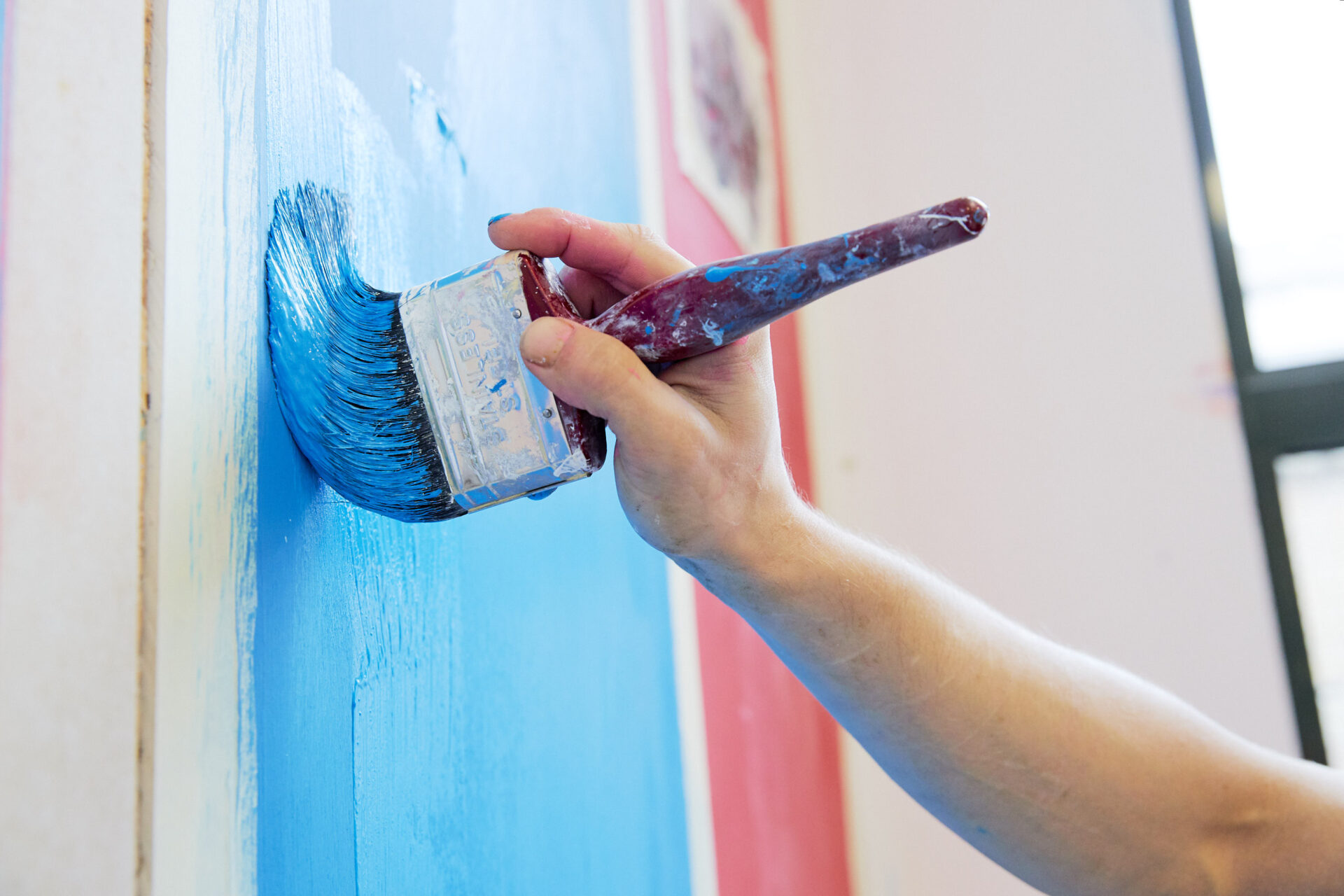 Hand holding a paint brush painting a wall blue